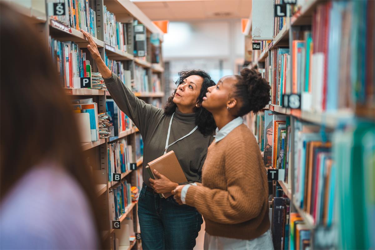 A librarian helps a patron locate a book in the library stacks.