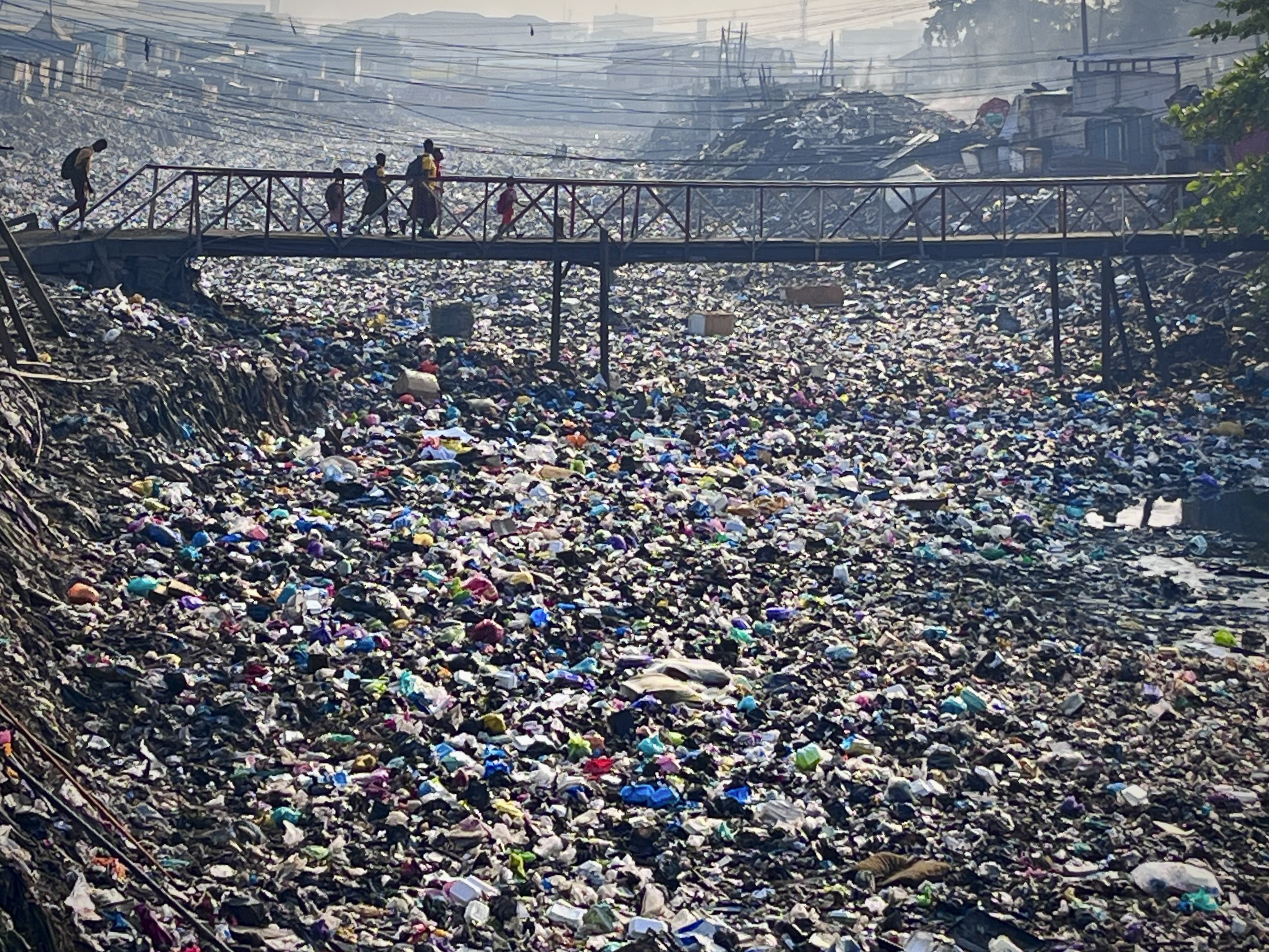 Children cross a bridge over a river clogged with plastic waste as they walk to school in Ghana's capital city.