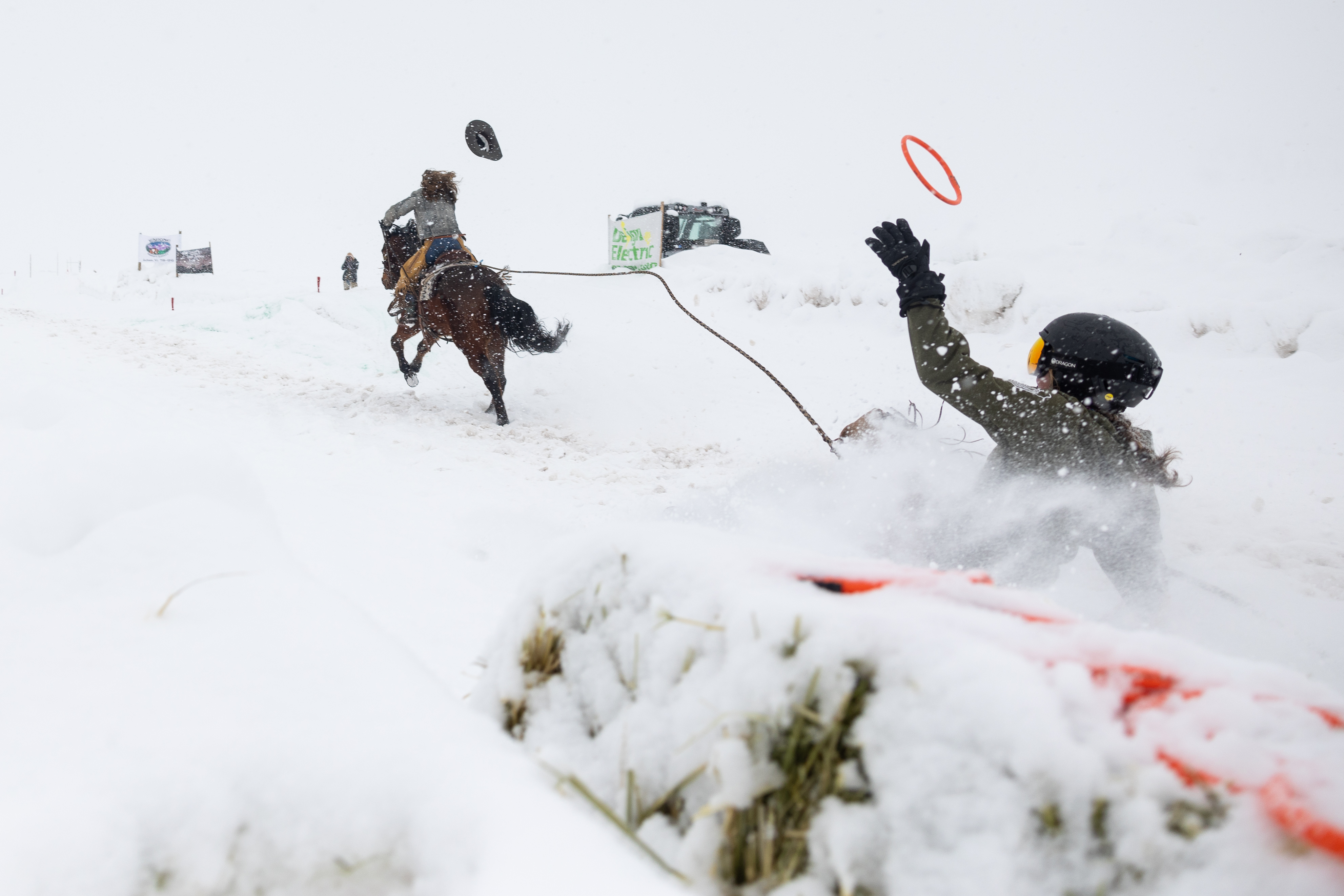 A skier reaches for one of the final rings on the course while being towed by a horse and rider during a skijoring competition. 