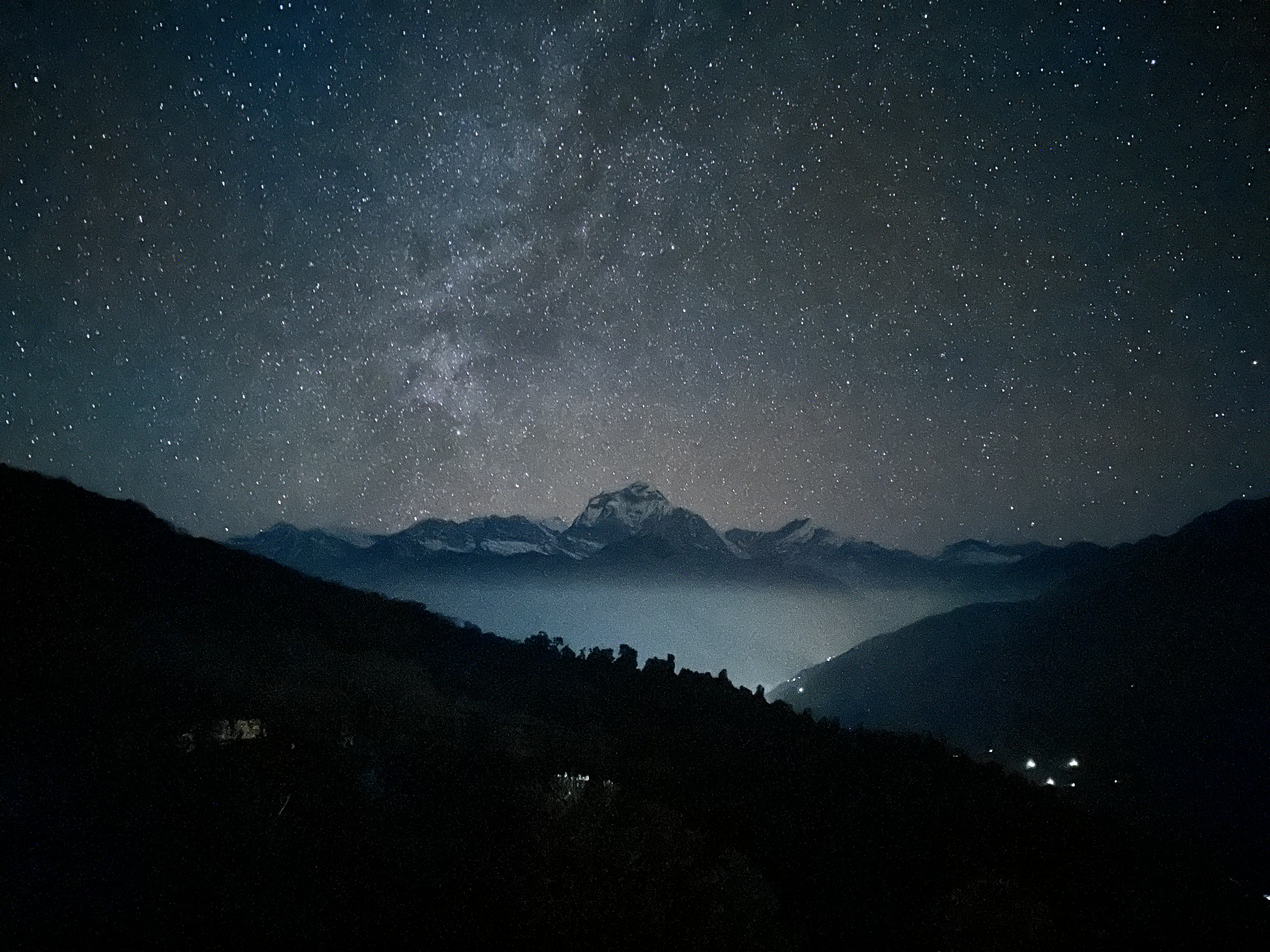 Star-filled night sky above a snowcapped mountain.
