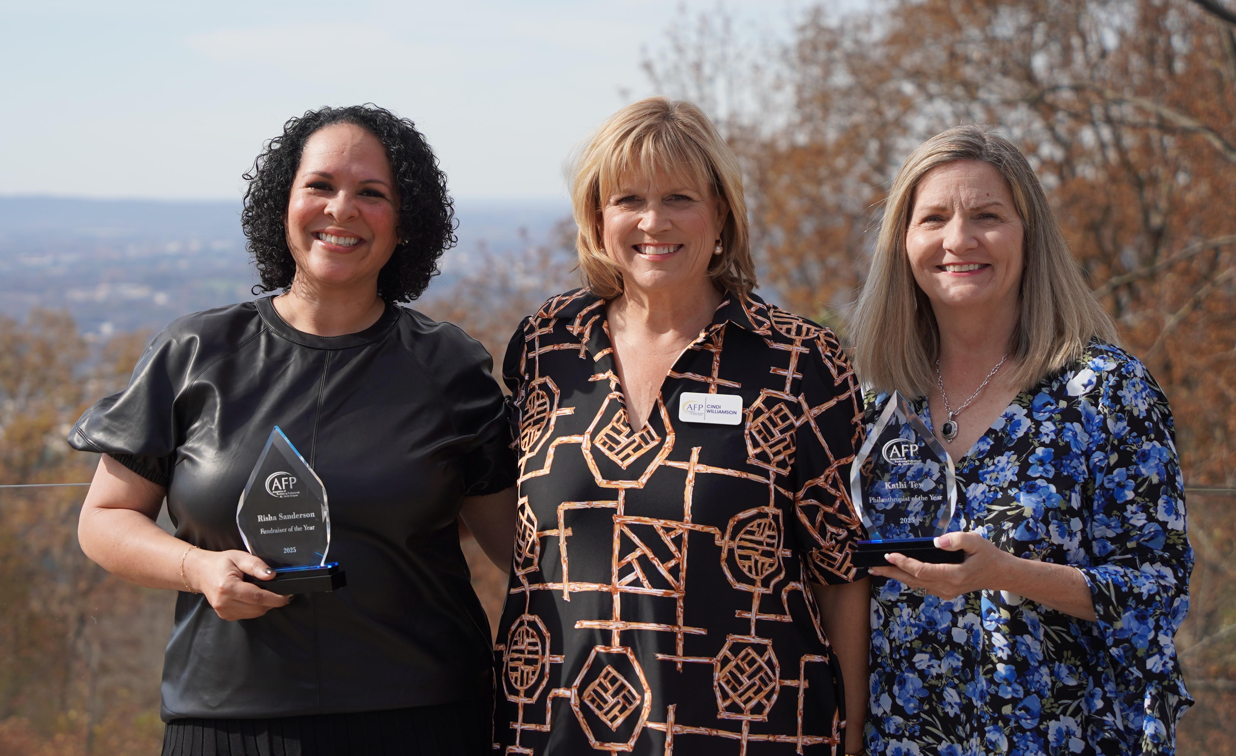 Three People in front of Burritt on the Mountain Overlook Smiling with two holding clear glass trophies.