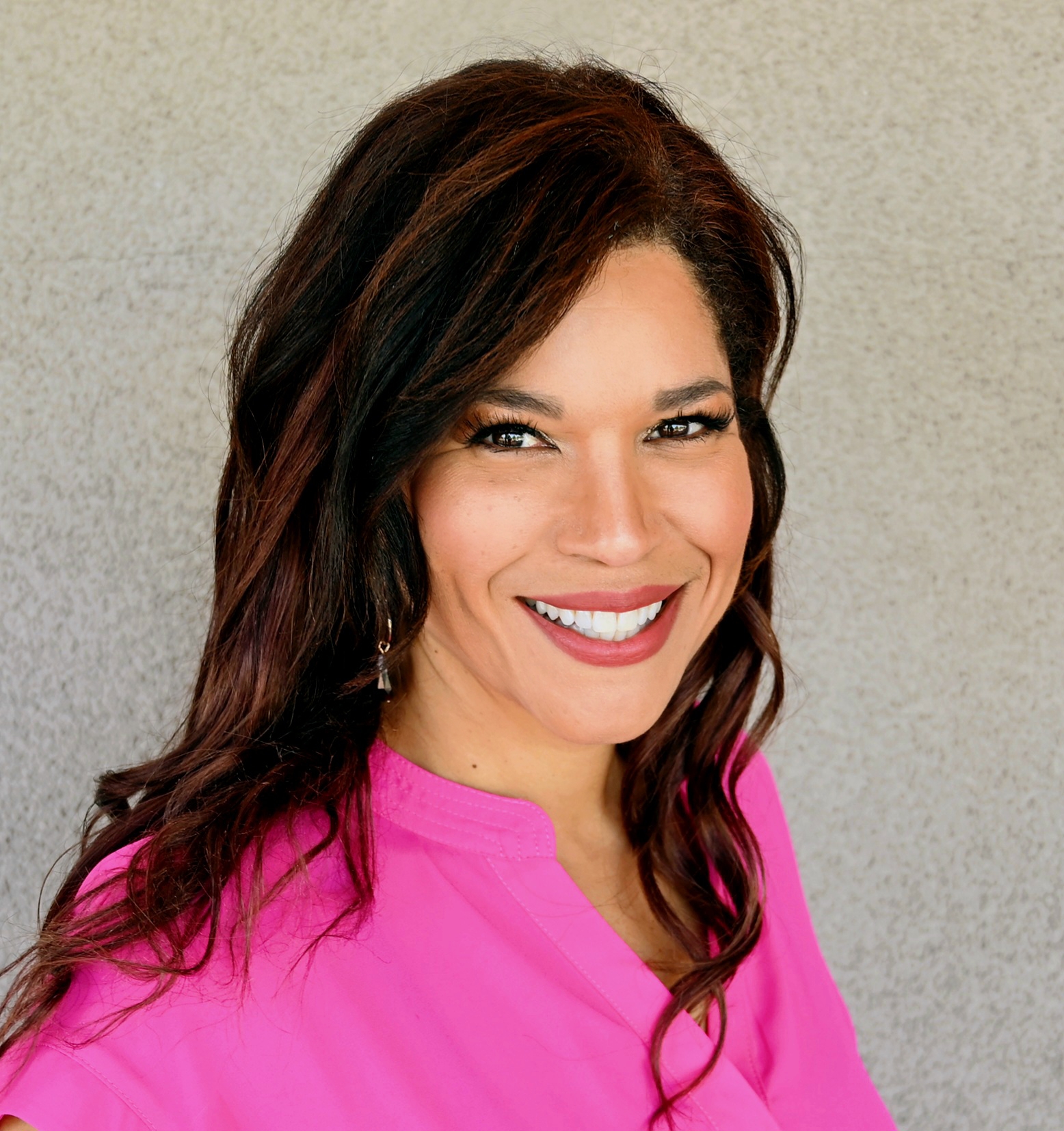 A smiling woman with long dark hair wearing a pink blouse