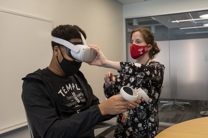 Carly Papenberg, director of Instructional Design at Temple University's Fox School of Business, assists Lawrence Ukenye with the placement of his Oculus headset.