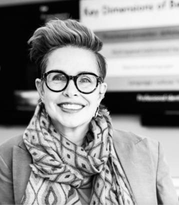 Dr. Bonnie Stewart, a smiling woman with round glasses and high wavy hair, wearing a large scarf and jacket. 