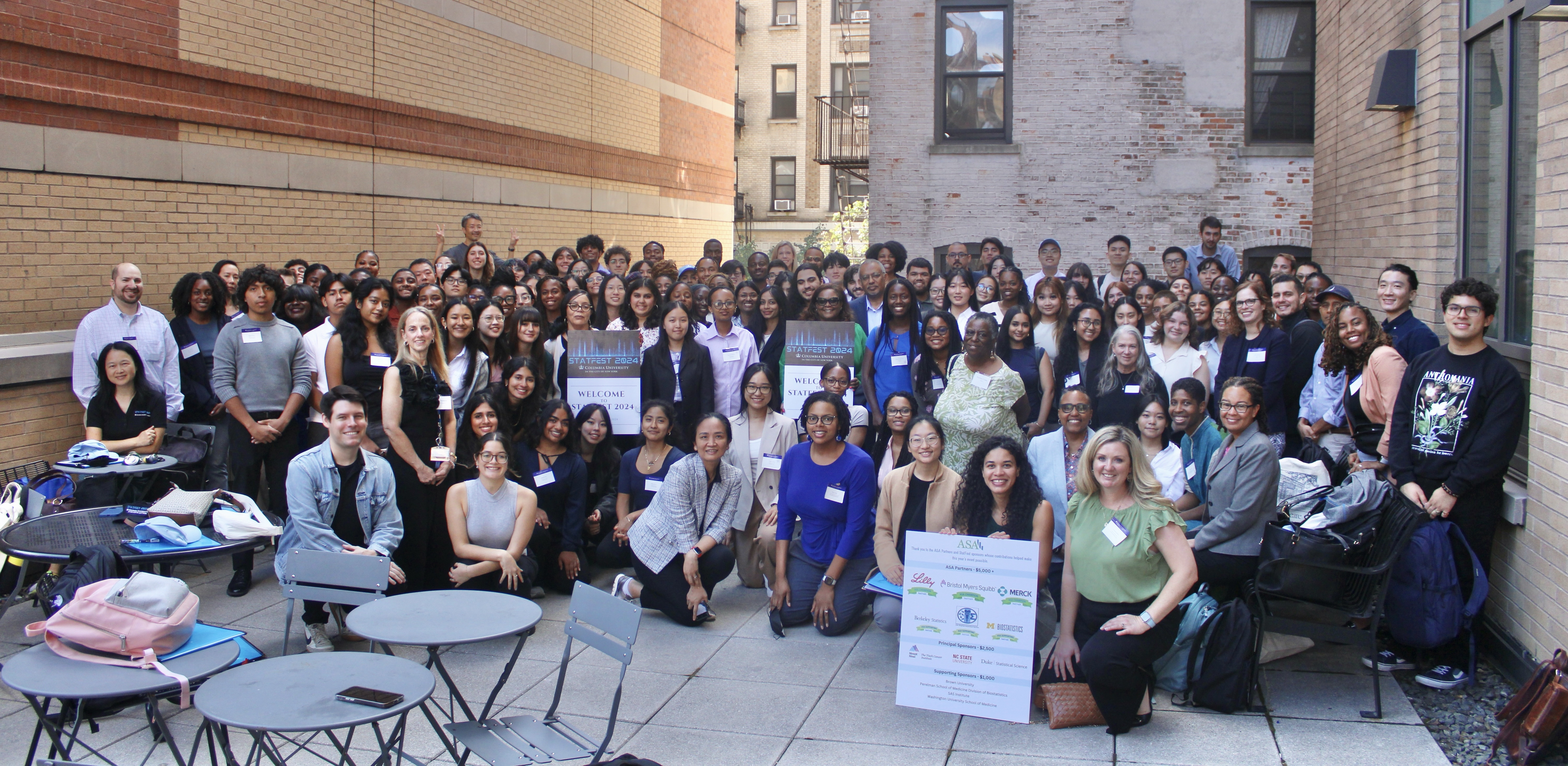 A diverse group of students and professionals gather for a group photo outside on a patio at Columbia University.