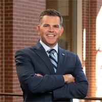 man in a grey suit smiles with arms crossed