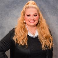 a woman with long blonde curly hair and wearing a dark suit smiles