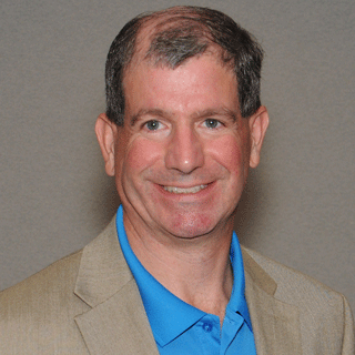 a man with a blue shirt and tan blazer smiles
