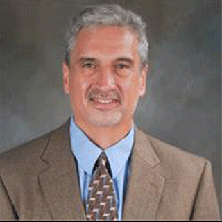 Man with white hair smiling wearing a tie and suit
