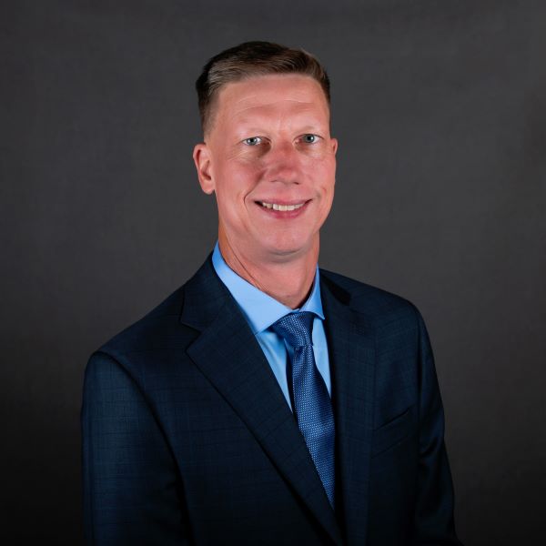 a man in a dark suit with a blue tie and blonde hair