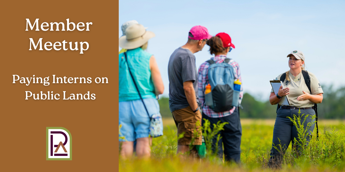 A young women wearing outdoor gear leads a tour of 6 adults through a field