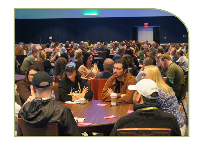 approximately 80 people sit around round tables of 8 in a large ballroom. each table is in discussion