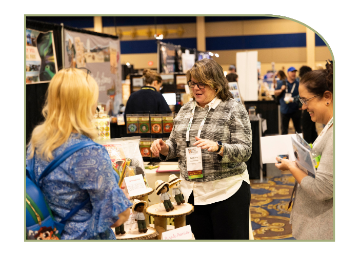 three women stand at a vendor booth displaying crocheted park ranger dolls