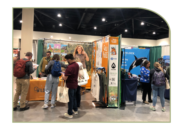 6 people mill around two vendor booths with nature themed clothes and mugs