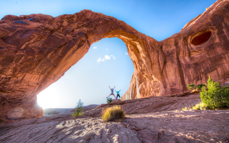 People jumping enthusiastically under a red rock arch