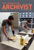 Two men lean over tables with documents in front of them, which they are wrapping in plastic wrap as part of a training course on disaster and emergency response at the Augsburg City Archive in 2016.