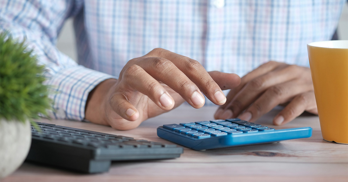 Person using a calculator and laptop to review healthcare payment data.