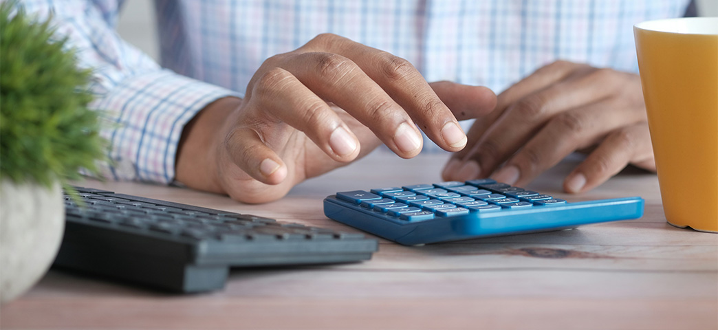 Person using a calculator and laptop to review healthcare payment data.
