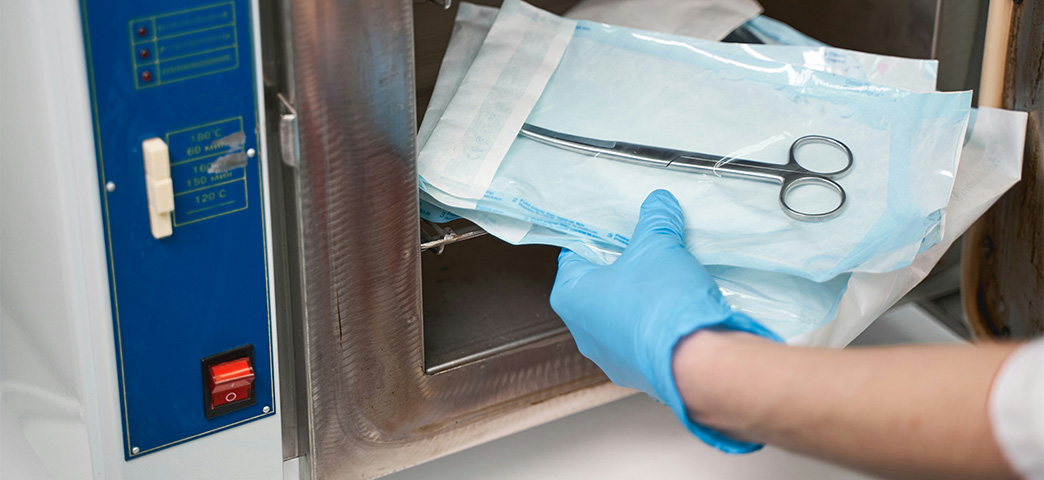 A medical professional placing sterilized equipment into a sterilizer.
