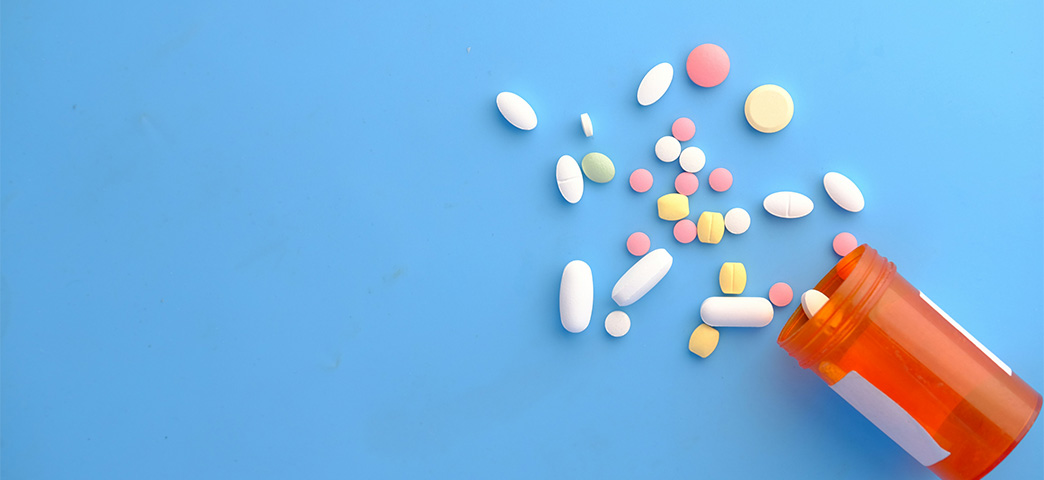 Pills spilling out from a medicine bottle on a blue surface.