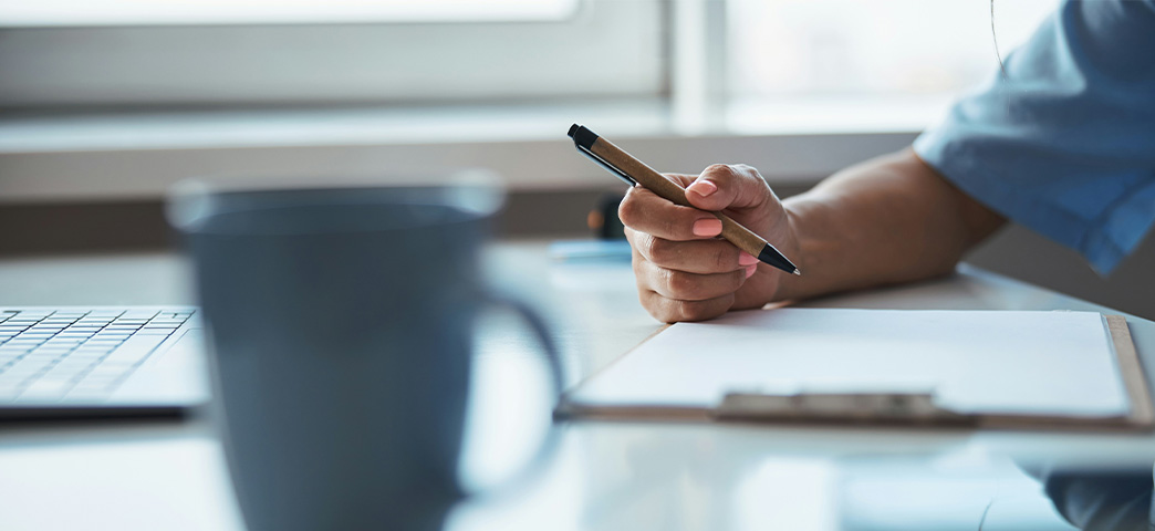 Healthcare professional writing notes on a clipboard at a desk.