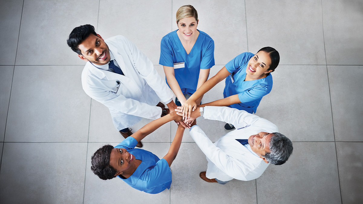 Medical professionals in a circle with stacked hands looking up at the camera.