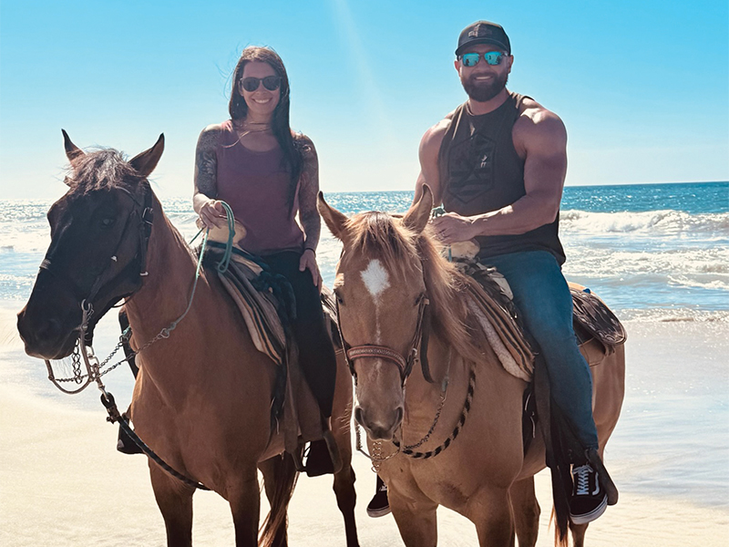 Kayli and her husband on horses at the beach.