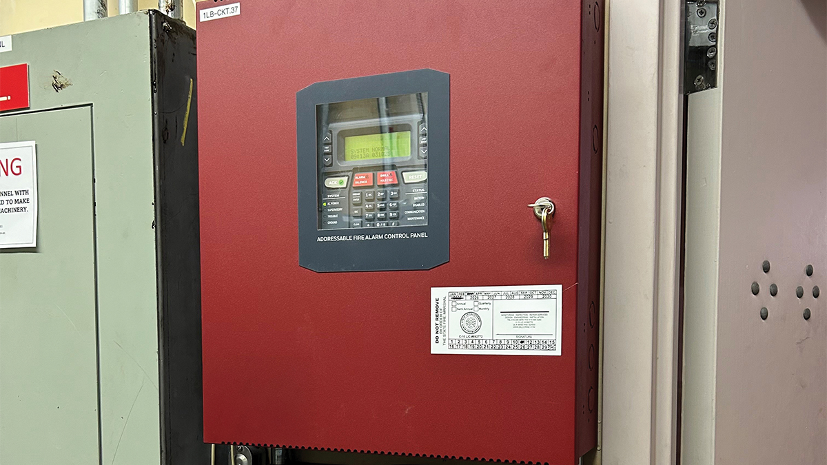 A red addressable fire alarm control panel mounted on a wall, displaying a normal system status