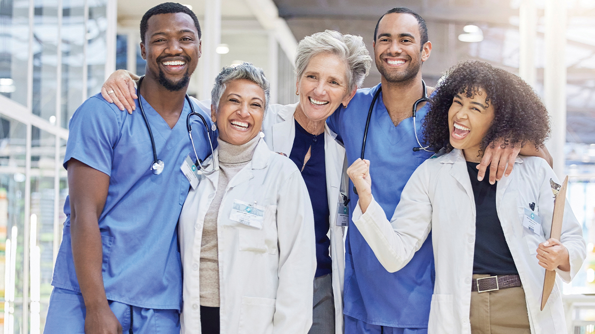  diverse group of five smiling healthcare professionals poses together in a clinical setting.
