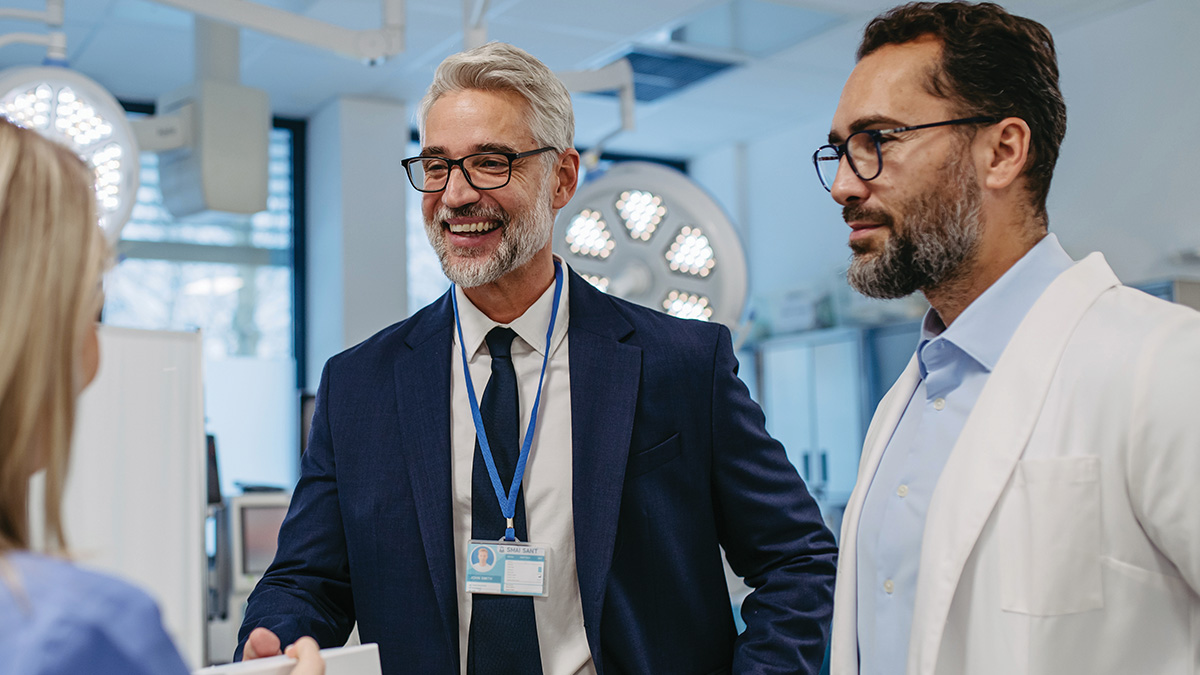 A surgery center administrator greets two colleagues during a facility tour in an operating room.
