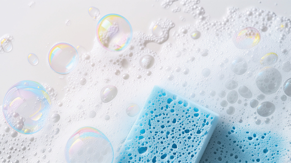 A blue sponge surrounded by soap suds and iridescent bubbles on a white surface.