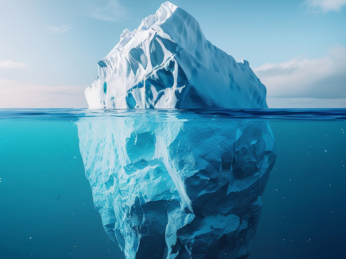 An iceberg shown above and below the waterline, with a small visible tip above the surface and a much larger mass submerged beneath the blue water.An iceberg shown above and below the waterline, with a small visible tip above the surface and a much larger mass submerged beneath the blue water.
