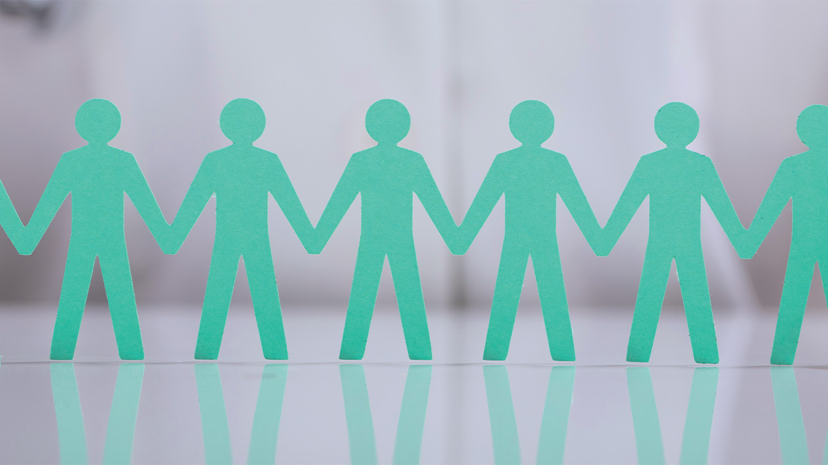 A row of green paper cutout figures holding hands on a white reflective surface.