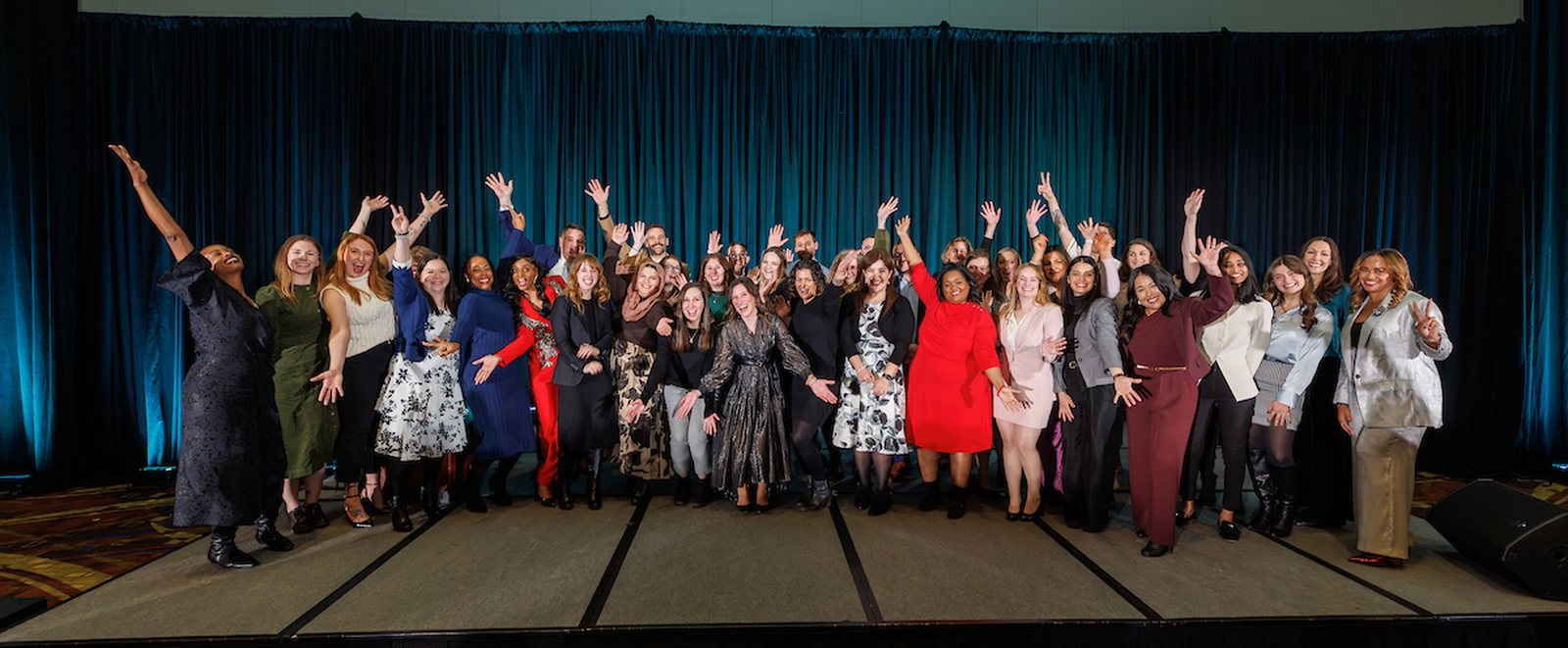 A large group of Association Forum members on stage with their arms raised