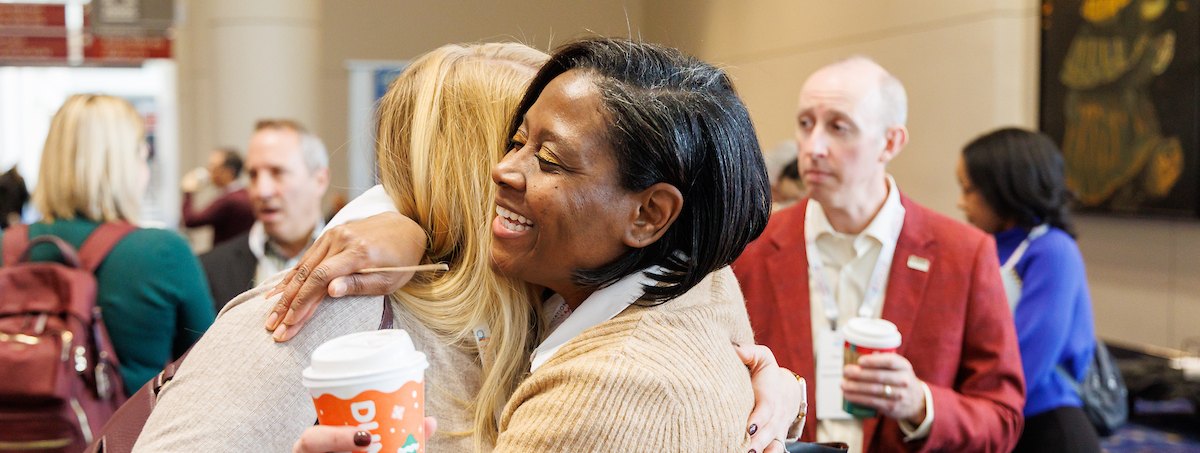 Two Association Forum members greeting each other with a hug at an event
