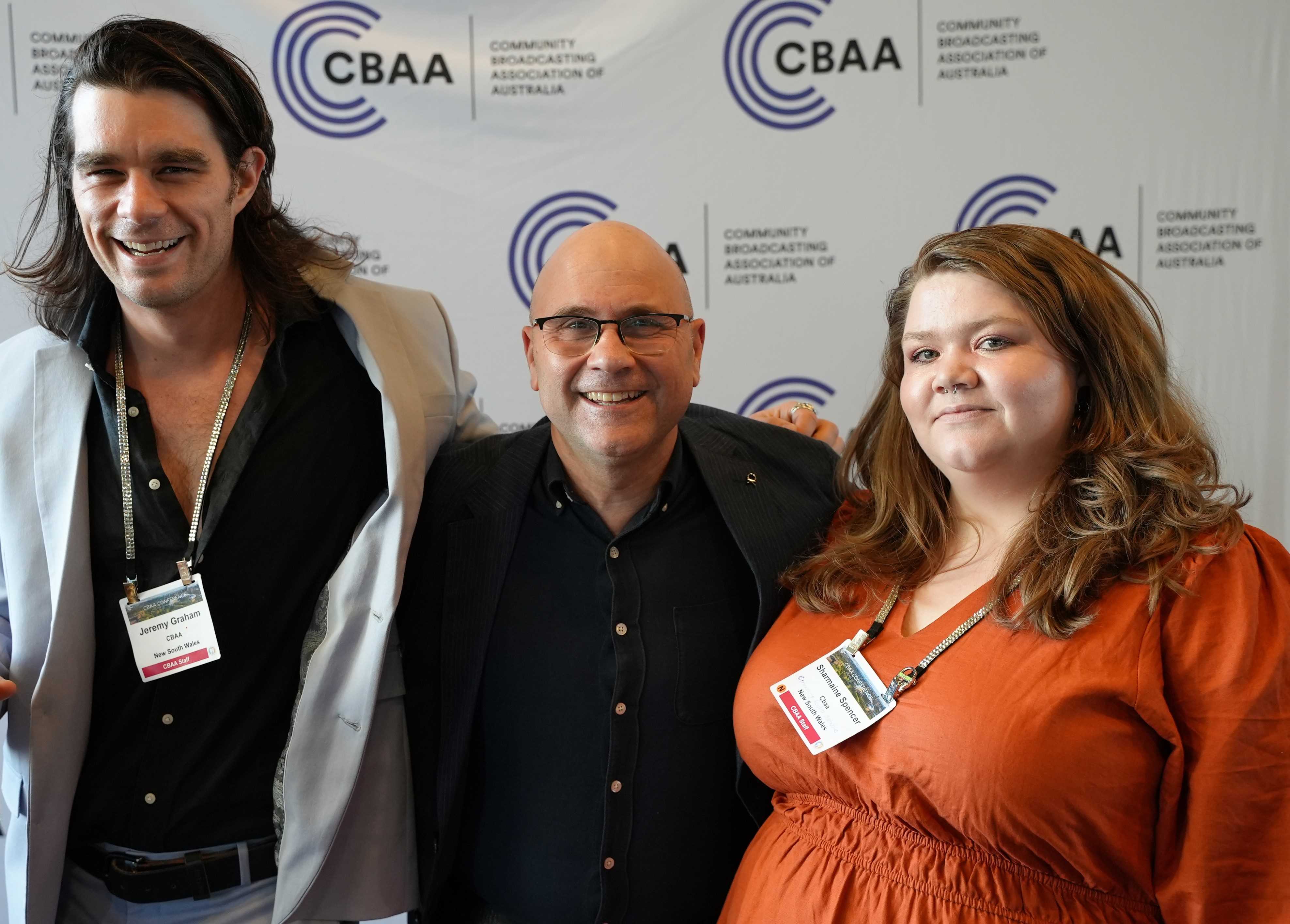 Three CBAA staff members in front of a media wall 