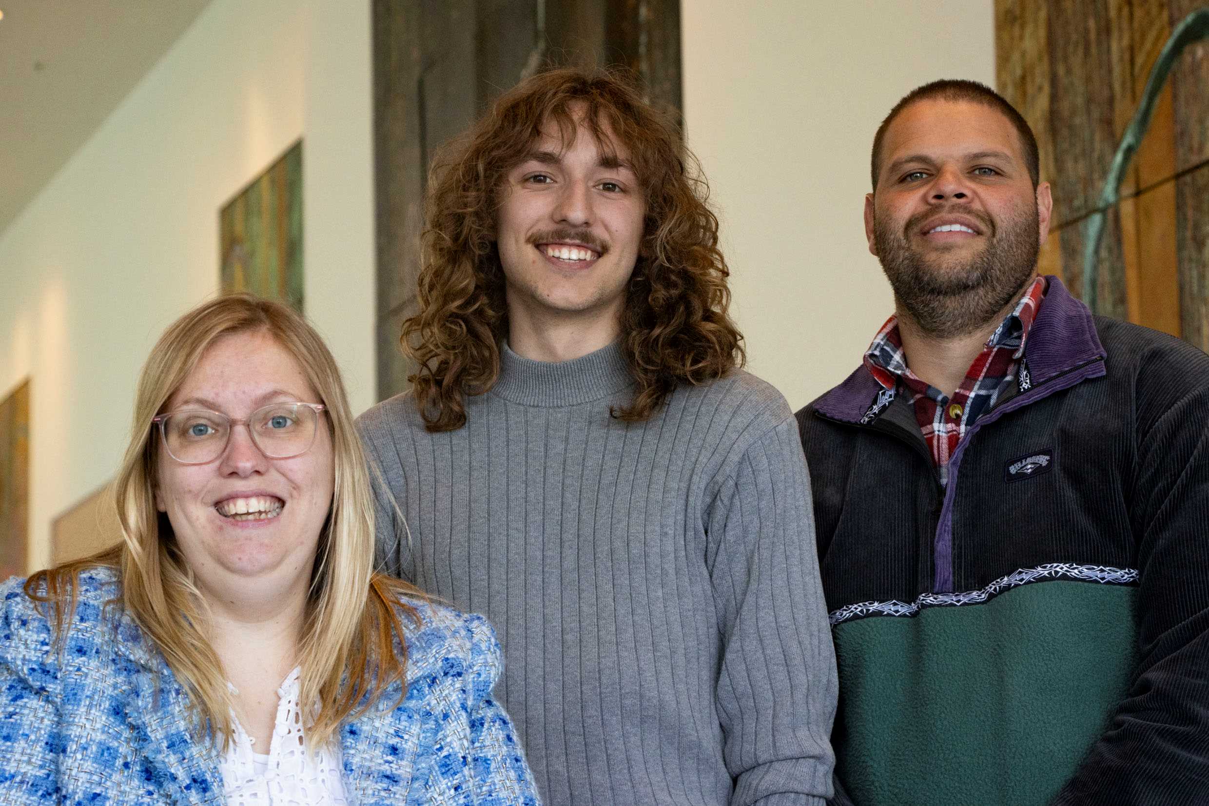 A woman and two men smiling at camera in a studio 