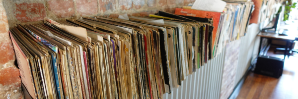 A row of old vinyl records on a shelf against a red brick wall 