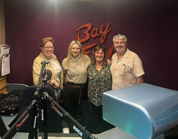 Four people posing in front of a Bay FM sign in a radio studio