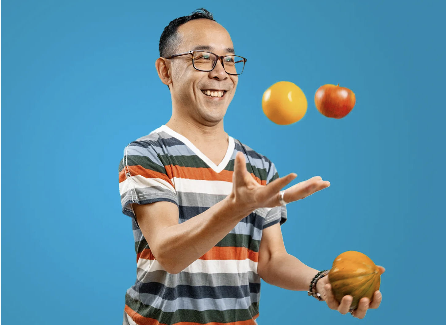 a smiling man in a striped shirt is juggling fruit