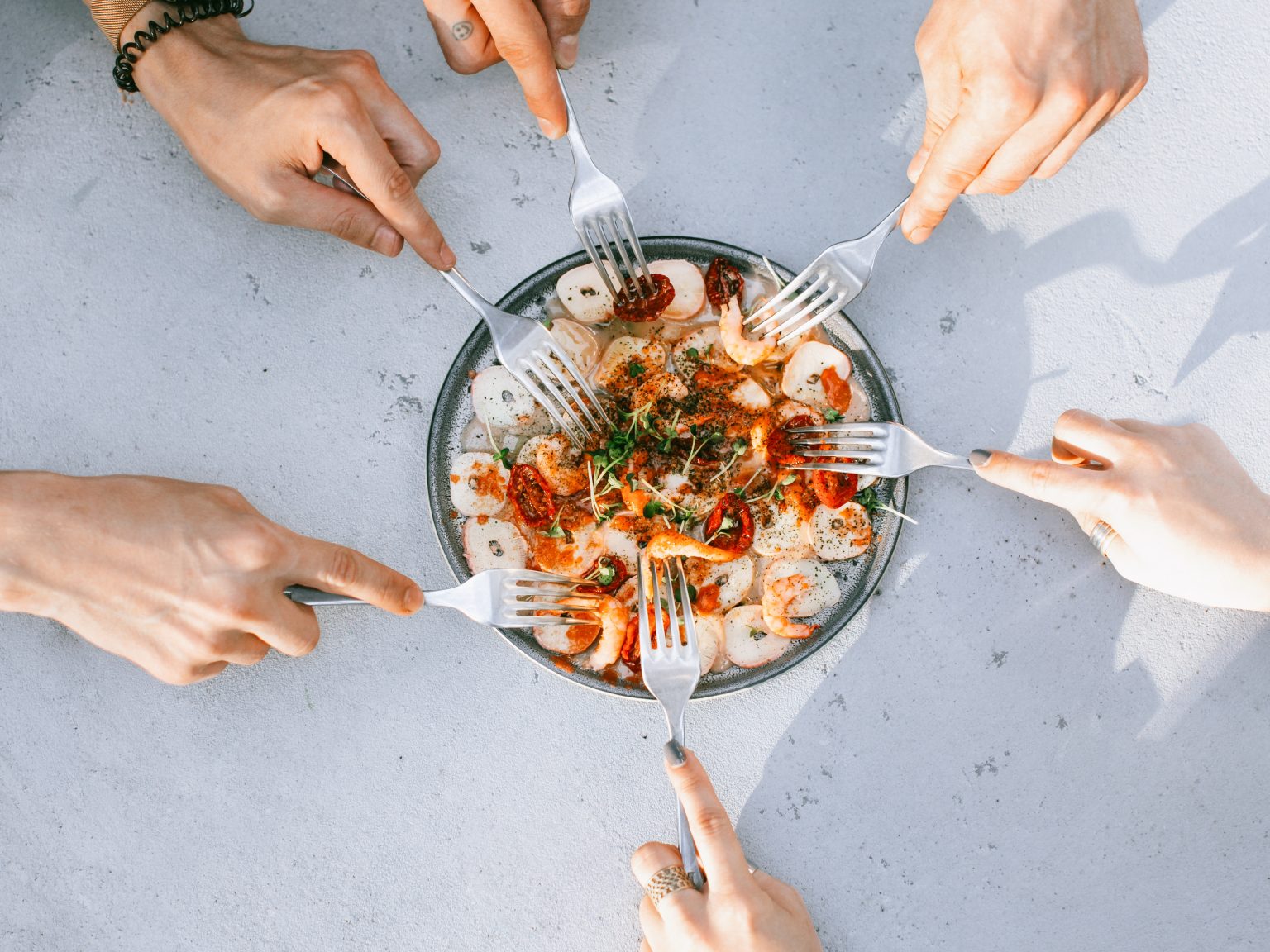 A group of hands using forks into a plate of shrimp.