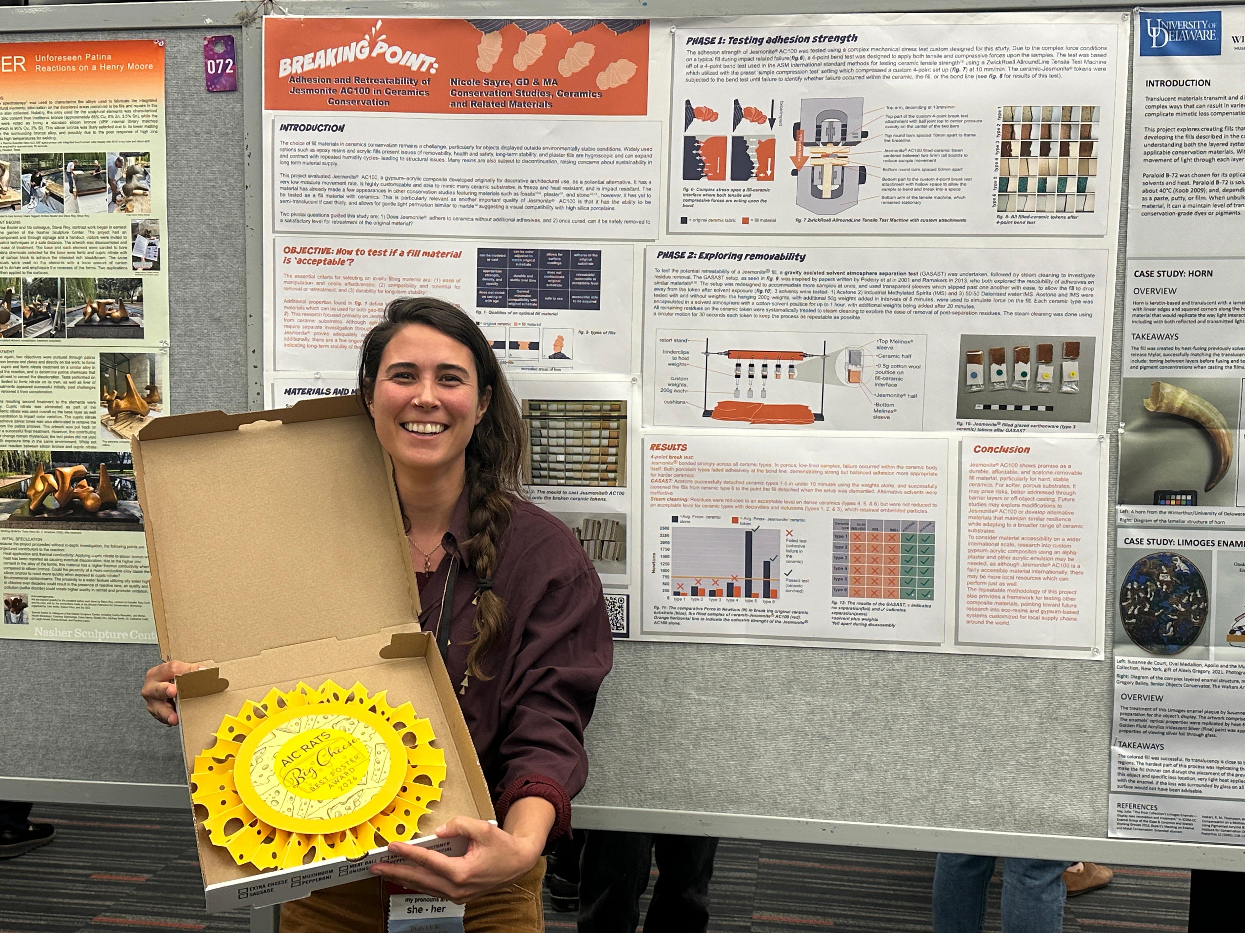 A smiling person holds a paper sculpture in the shape of a Swiss cheese wheel as a poster award prize