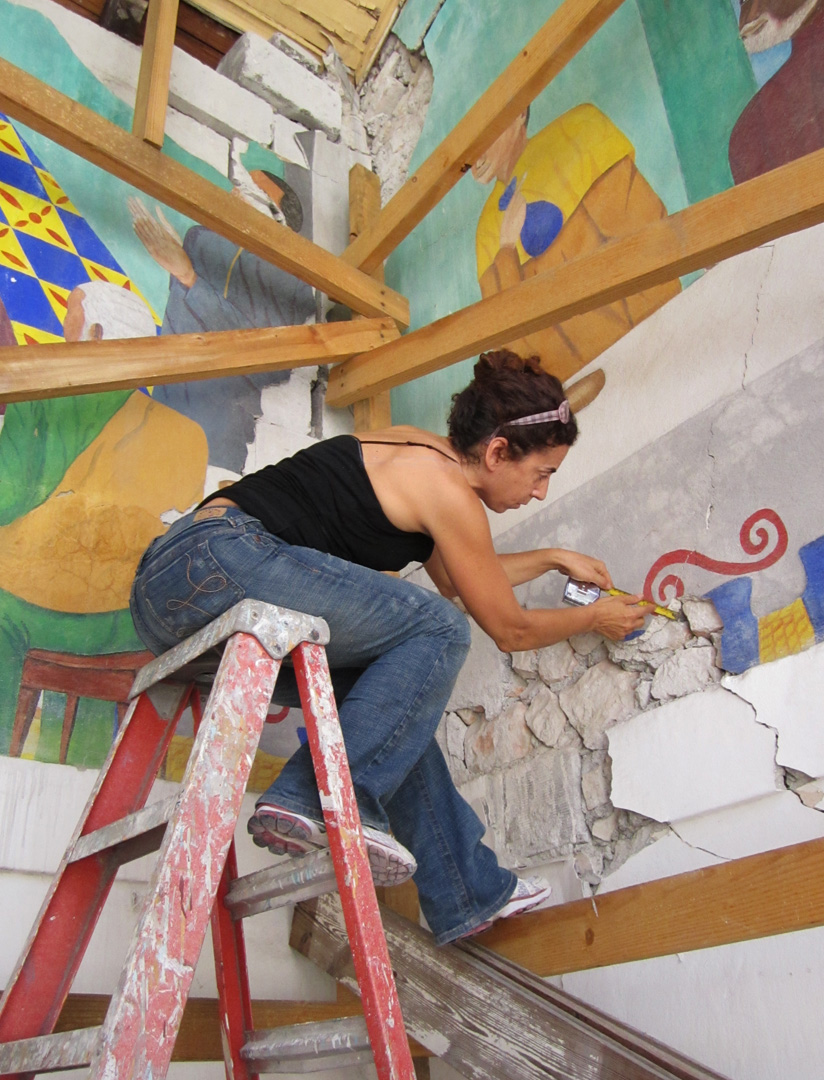 Woman on ladder measuring damage to a mural.