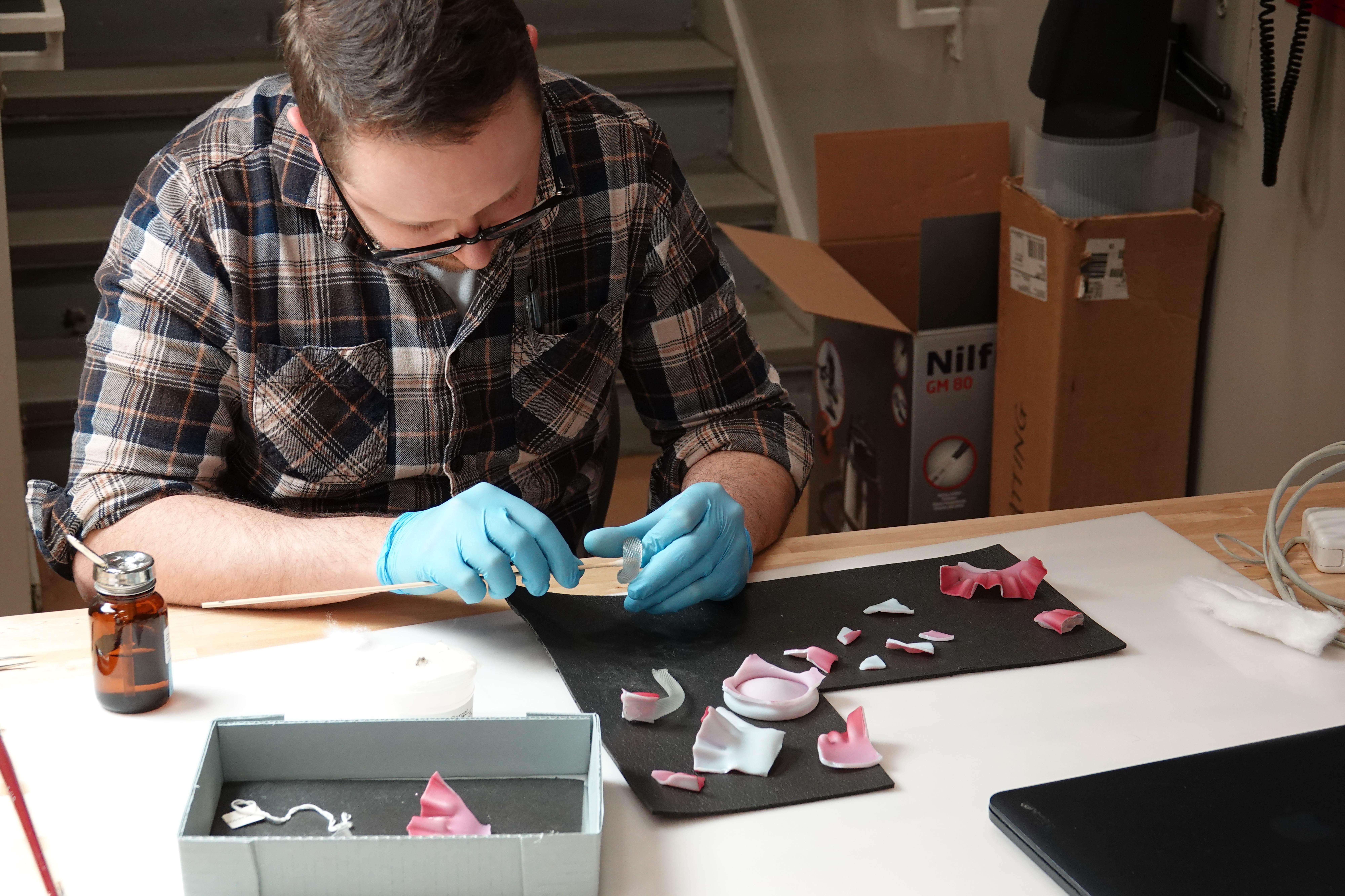 A conservator works on a white and pink candy dish that is broken into several pieces