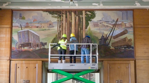 Three people on a scissor lift examining a mural