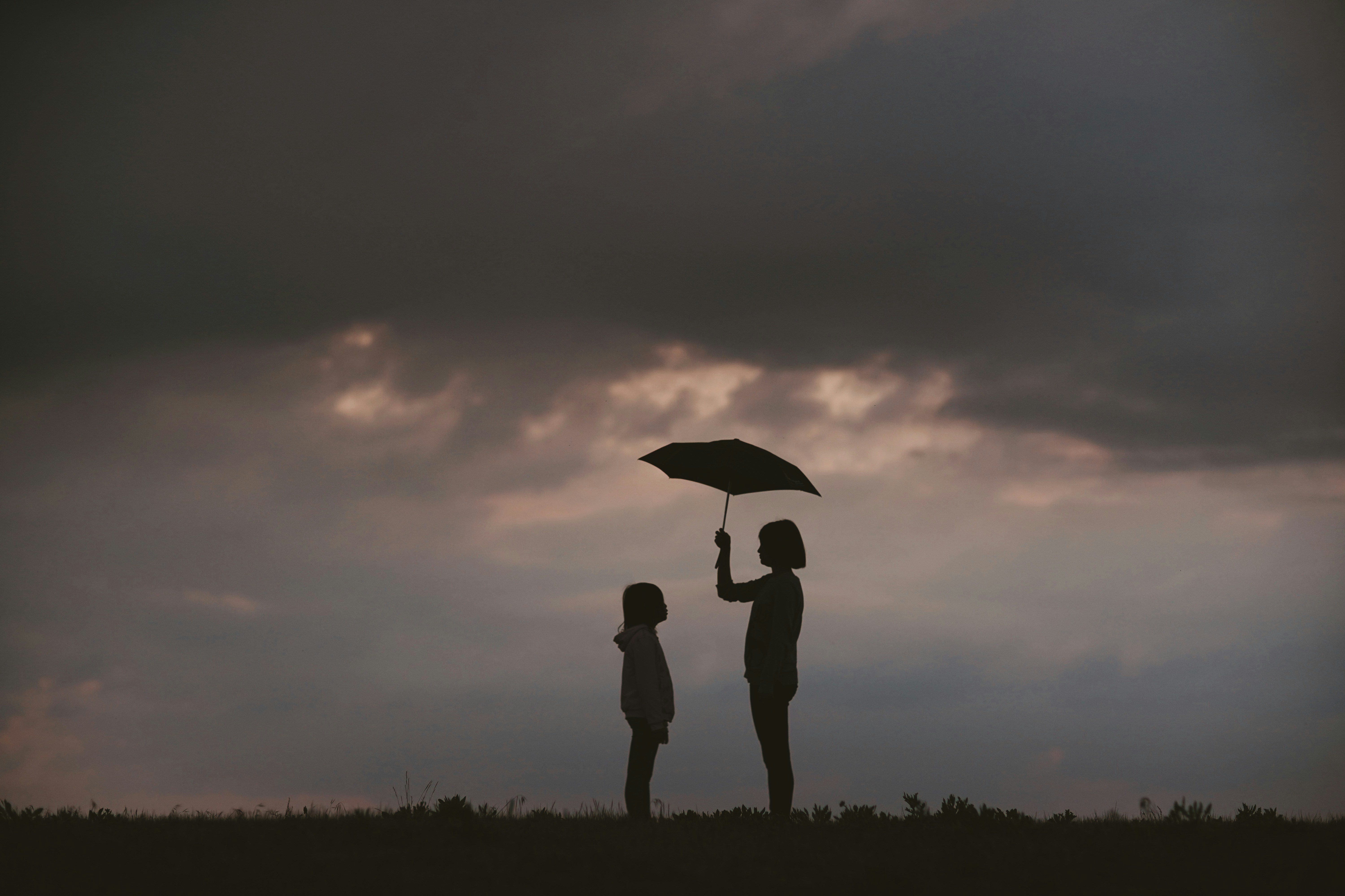 Two people in silhouette, one holding an umbrella over the other