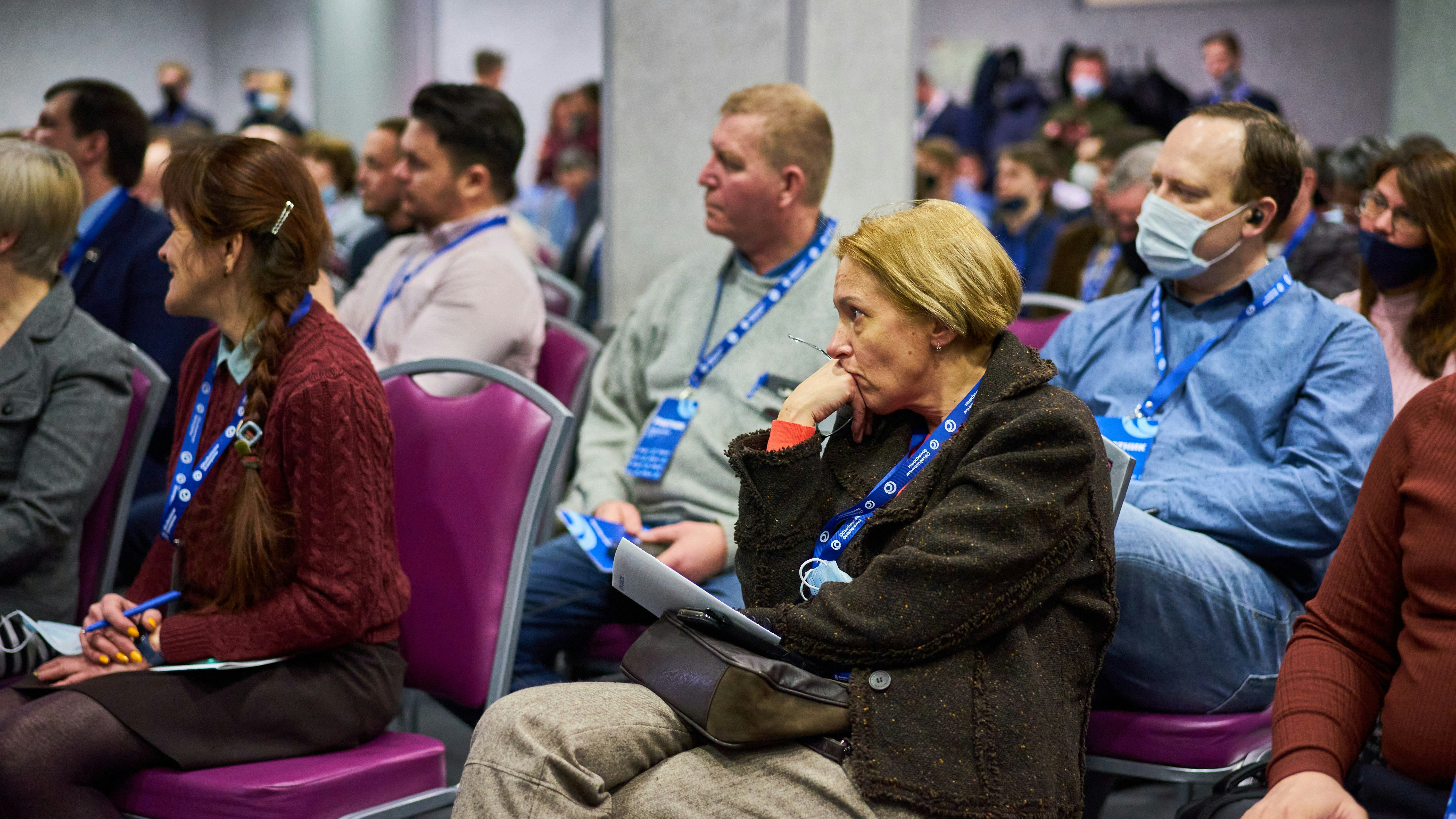 People wearing lanyards sitting in a room watching a presentatio