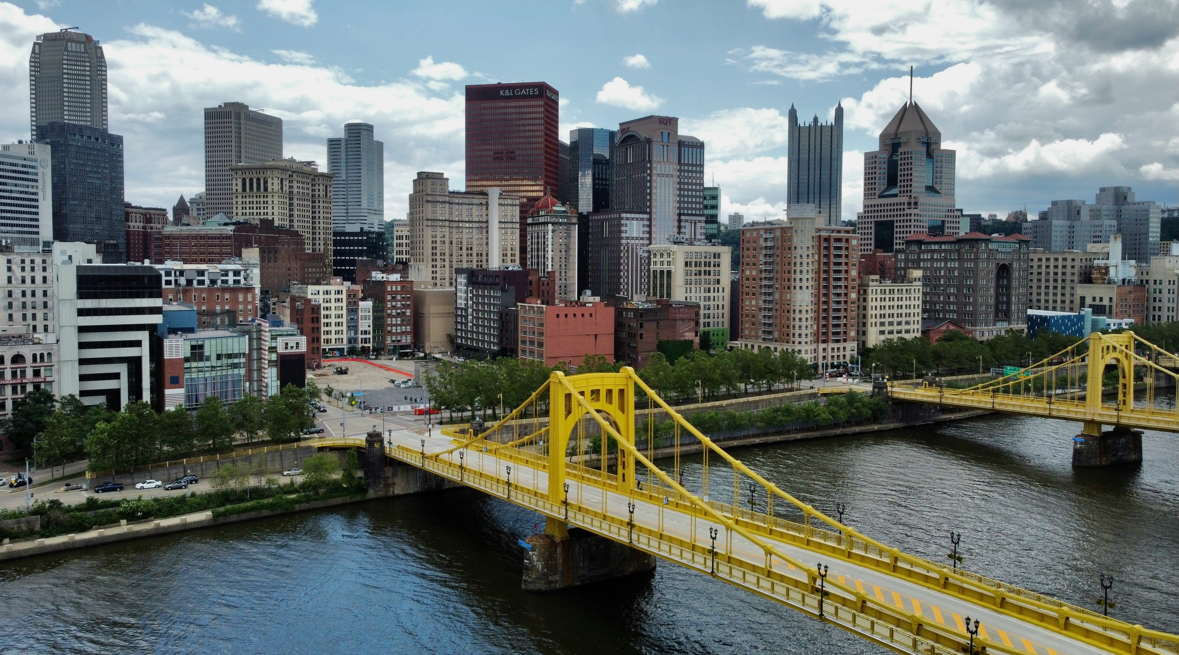Two yellow suspension bridges over river with city buildings