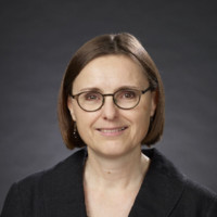 Headshot of a woman with short brown hair wearing a black jacket and glasses