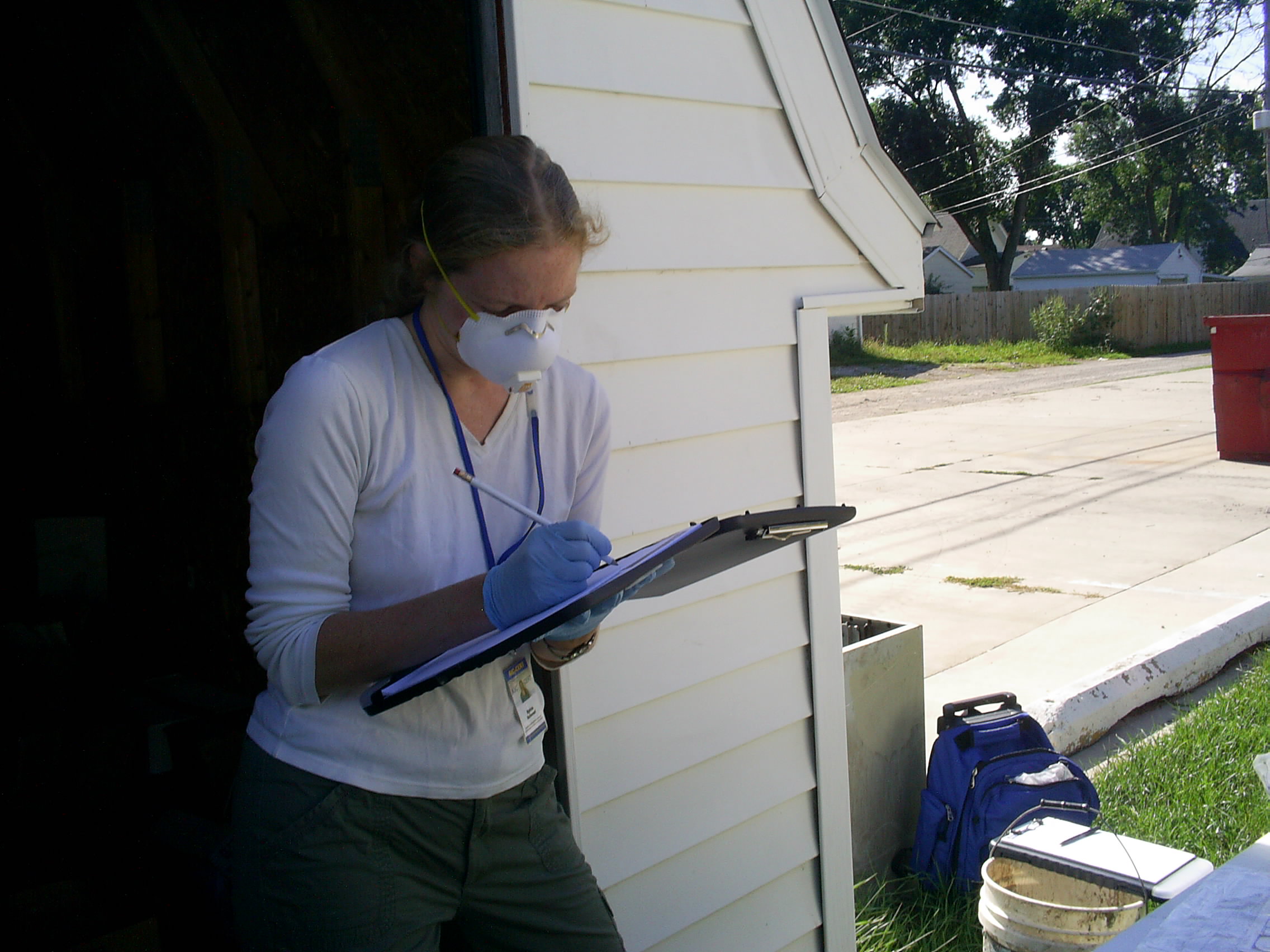 Woman wearing mask, holding clipboard.